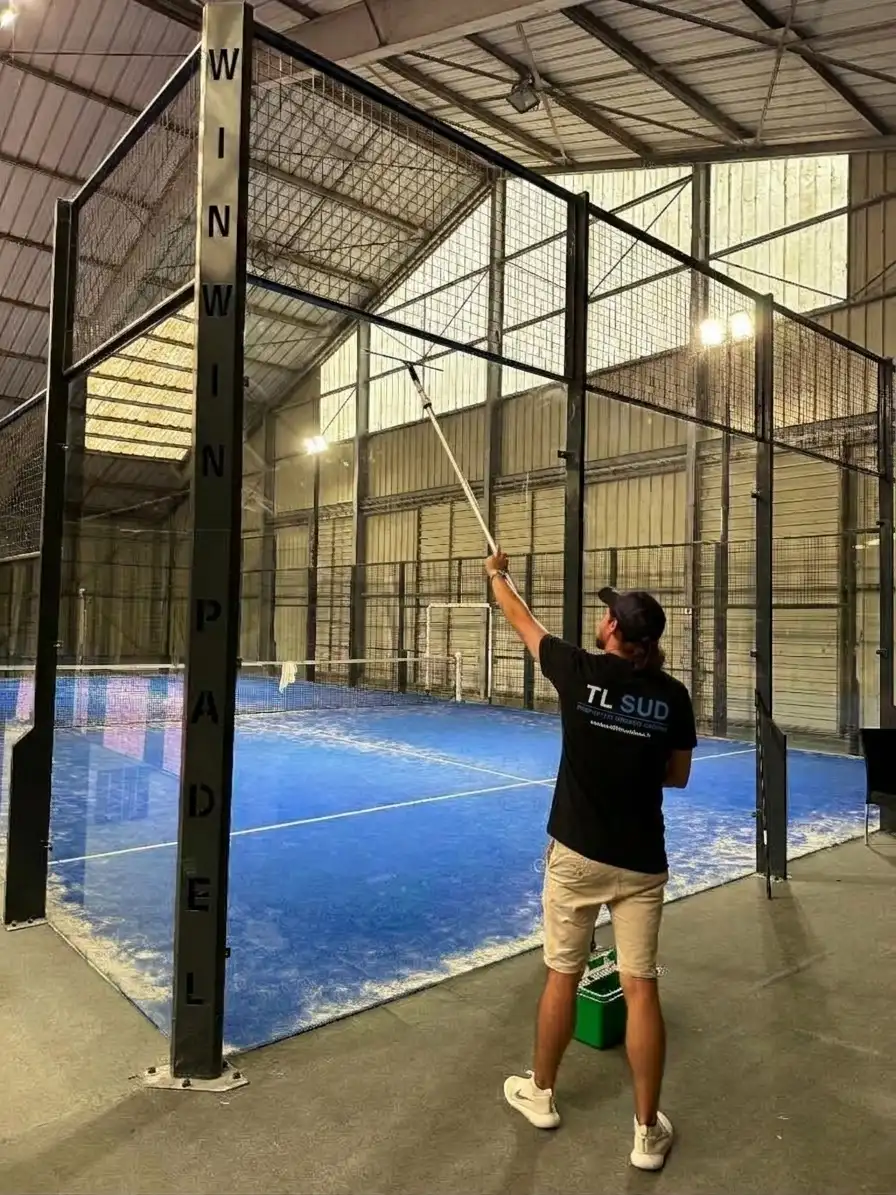 Agent TL SUD nettoyant à la perche les parois vitrées d’un terrain de padel couvert
